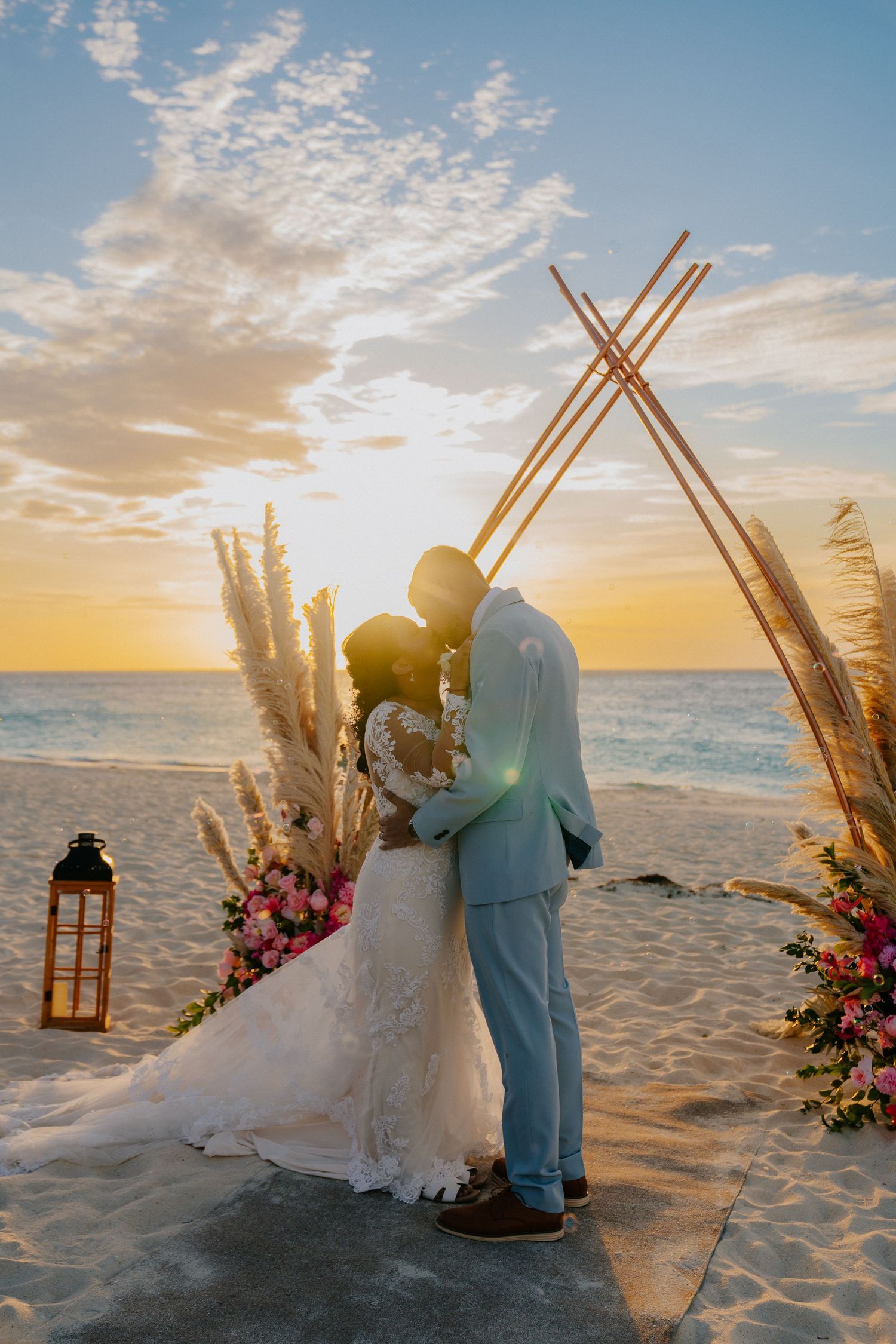 A beach wedding ceremony setup with bamboo arch and floral arrangements at sunset.