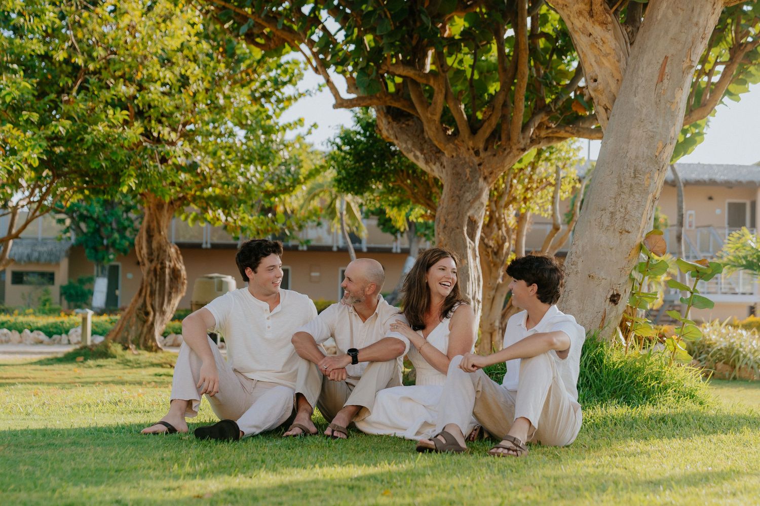 A group relaxes under the shade of large tropical trees on a grassy lawn.