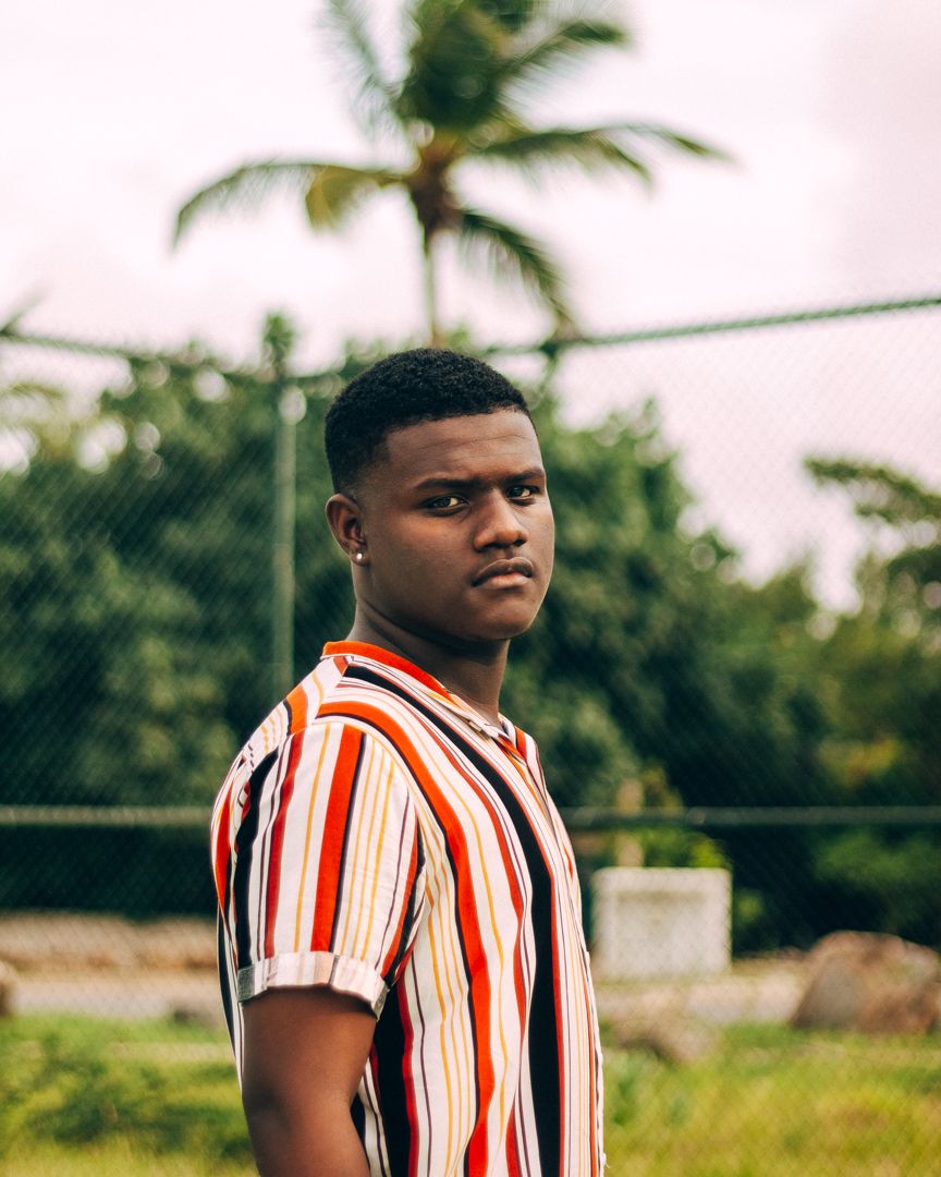 Man in striped shirt posing outdoors with palm trees in background.