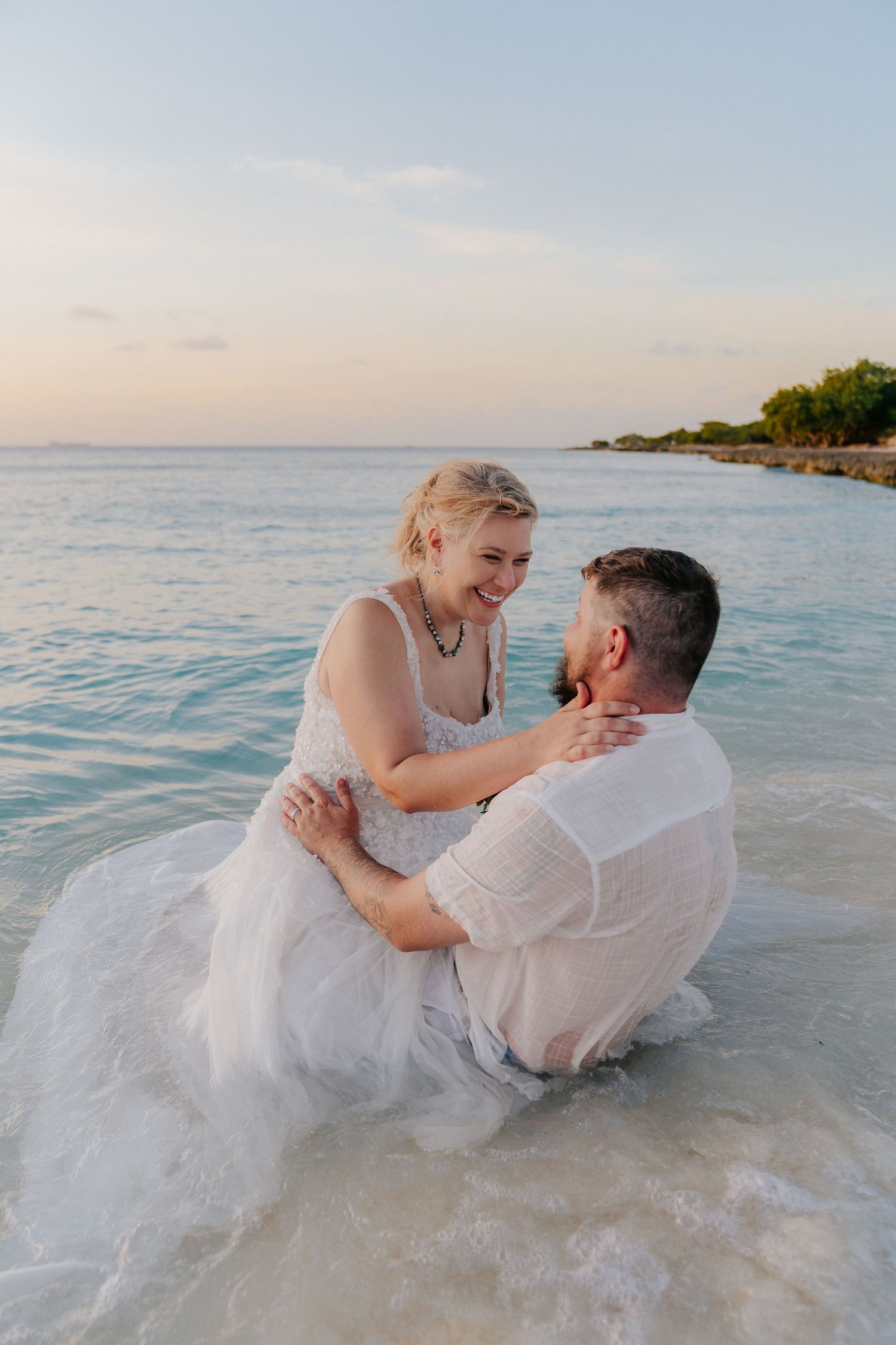 Newlyweds playing in the ocean water during sunset, creating a joyful moment.