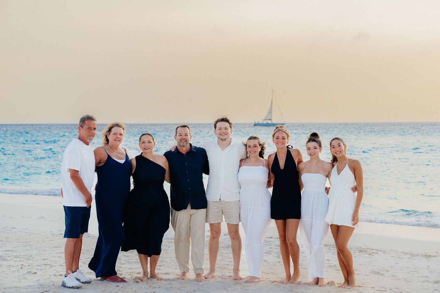 Extended family poses together on a beautiful beach at sunset wearing matching white and black attire.