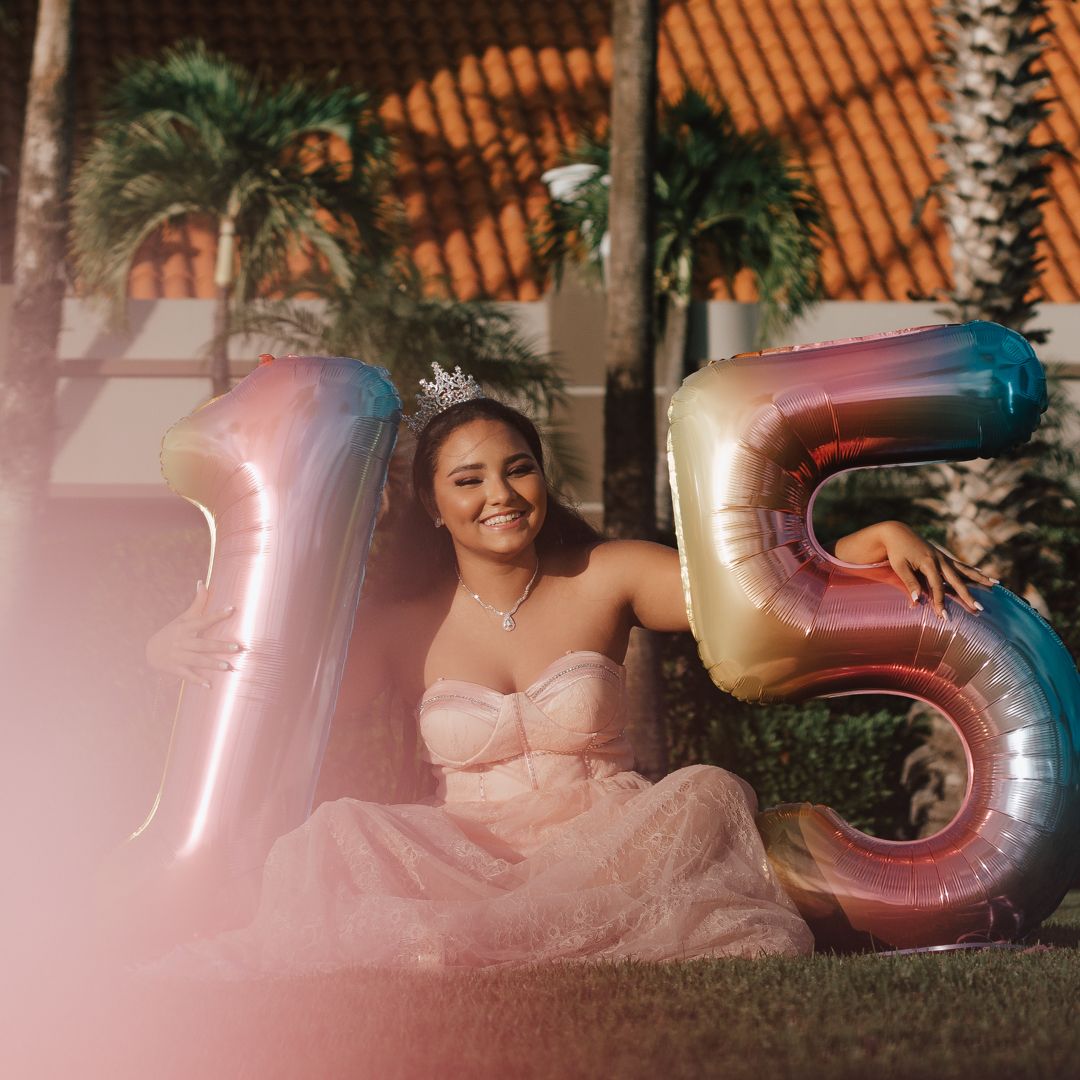 Pink and silver number balloons arranged for celebration with palm trees in background.