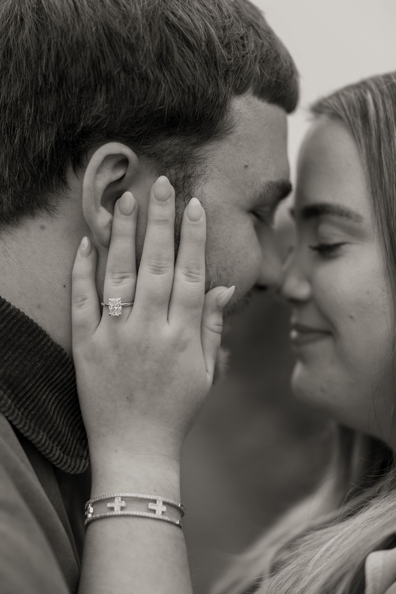 Black and white photo of a couple sharing a romantic moment, woman showing engagement ring on hand.