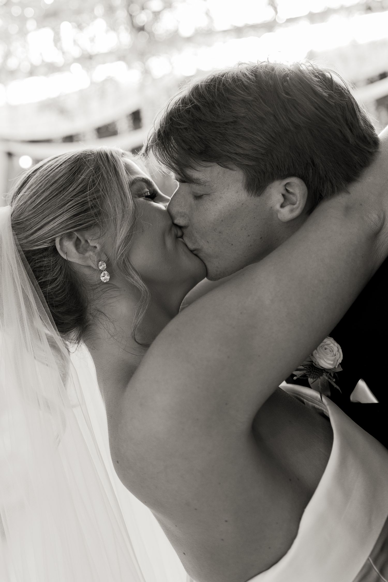 Black and white photo of a bride and groom sharing a romantic first kiss at their wedding ceremony.