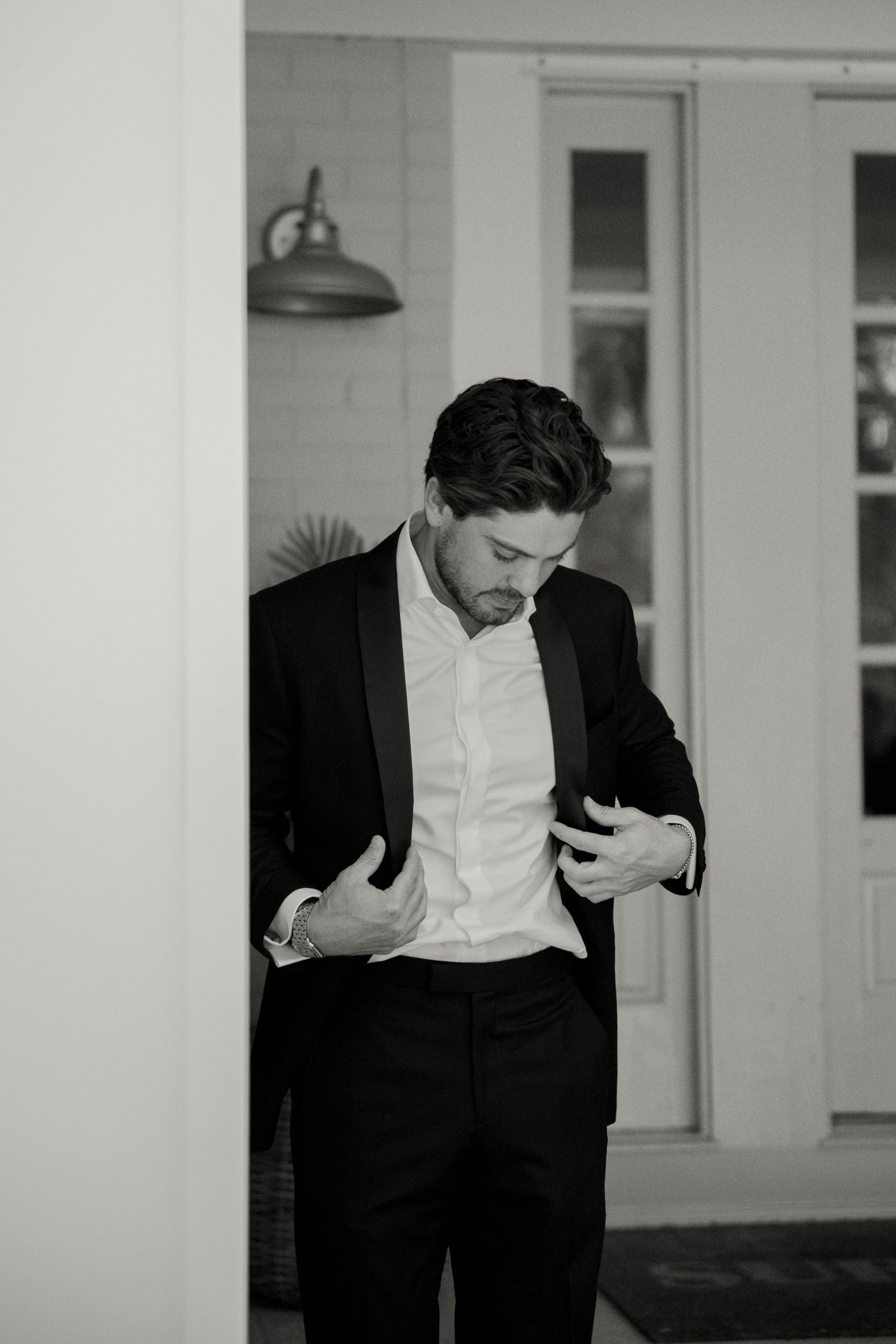Black and white photo of a well-dressed groom in a tuxedo adjusting his jacket before his wedding ceremony.