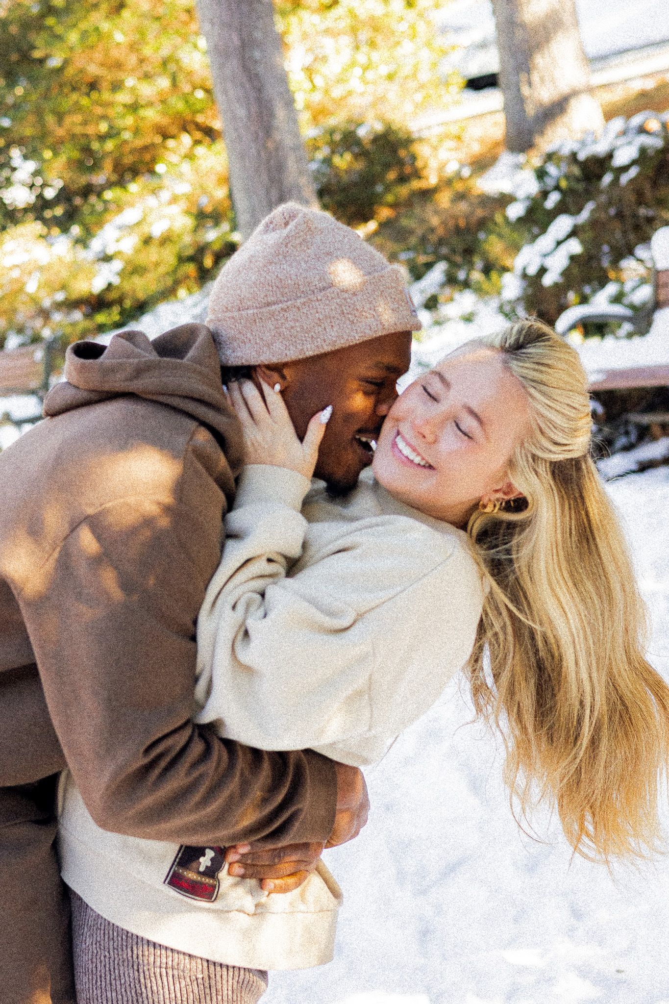 A joyful interracial couple embracing and laughing together outdoors in a snowy winter setting.