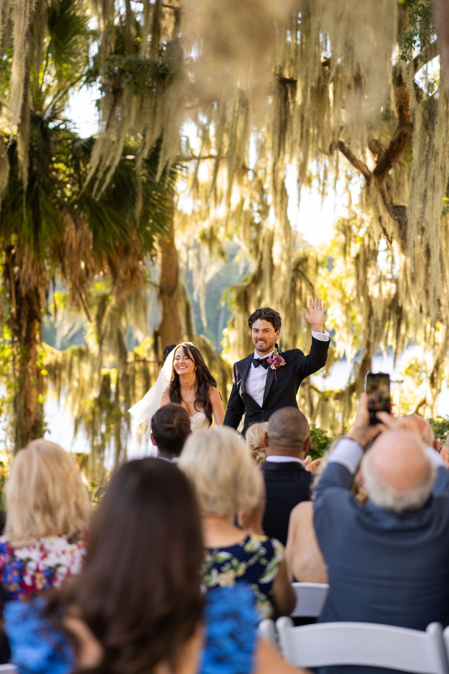 Bride and groom walk down the aisle under Spanish moss-draped oak trees at an outdoor wedding ceremony.