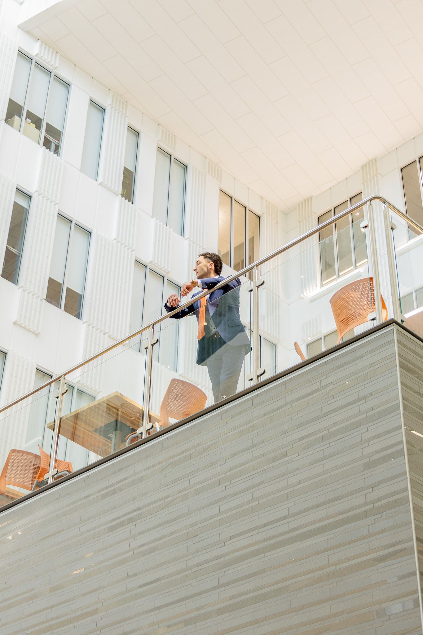 Businessman in suit standing on modern office building balcony with glass railing, talking on phone.