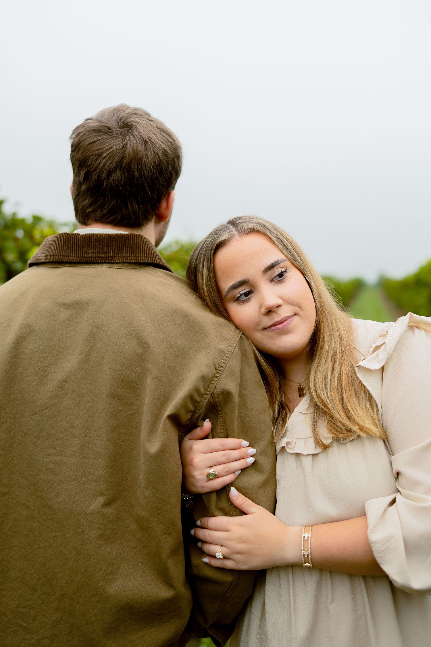Young woman in cream blouse resting her head on a man's shoulder outdoors, smiling softly at the camera.