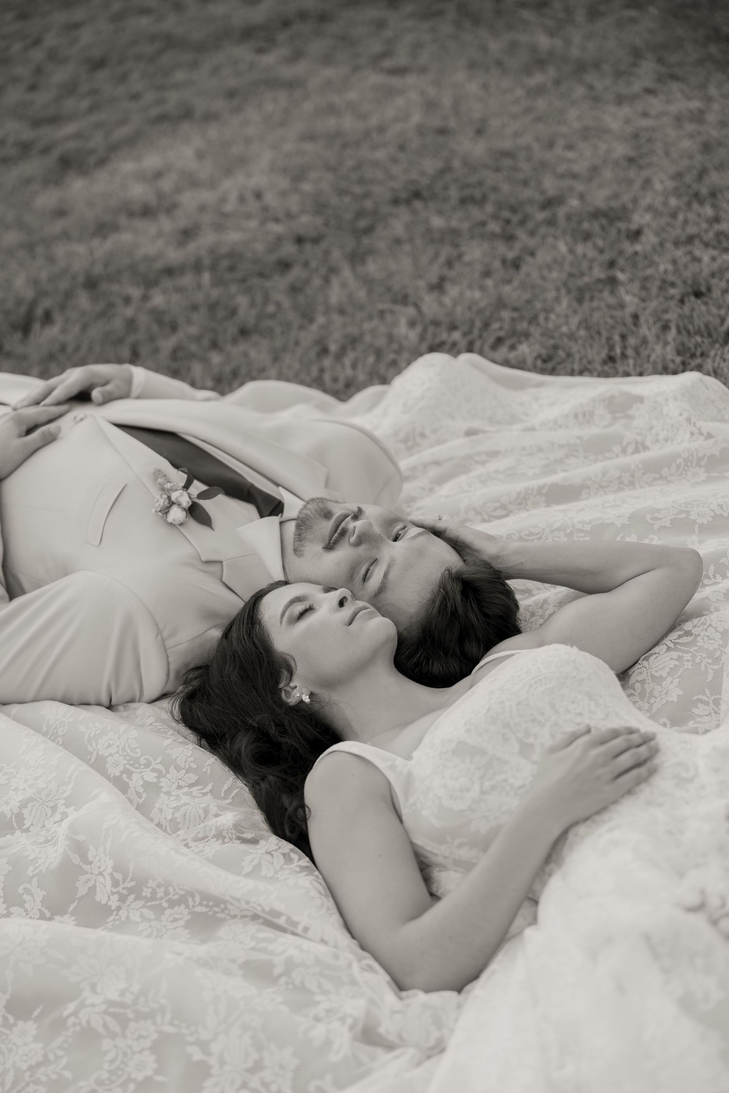 Three women in elegant dresses lying on a blanket in grass, laughing together in a black and white photo.