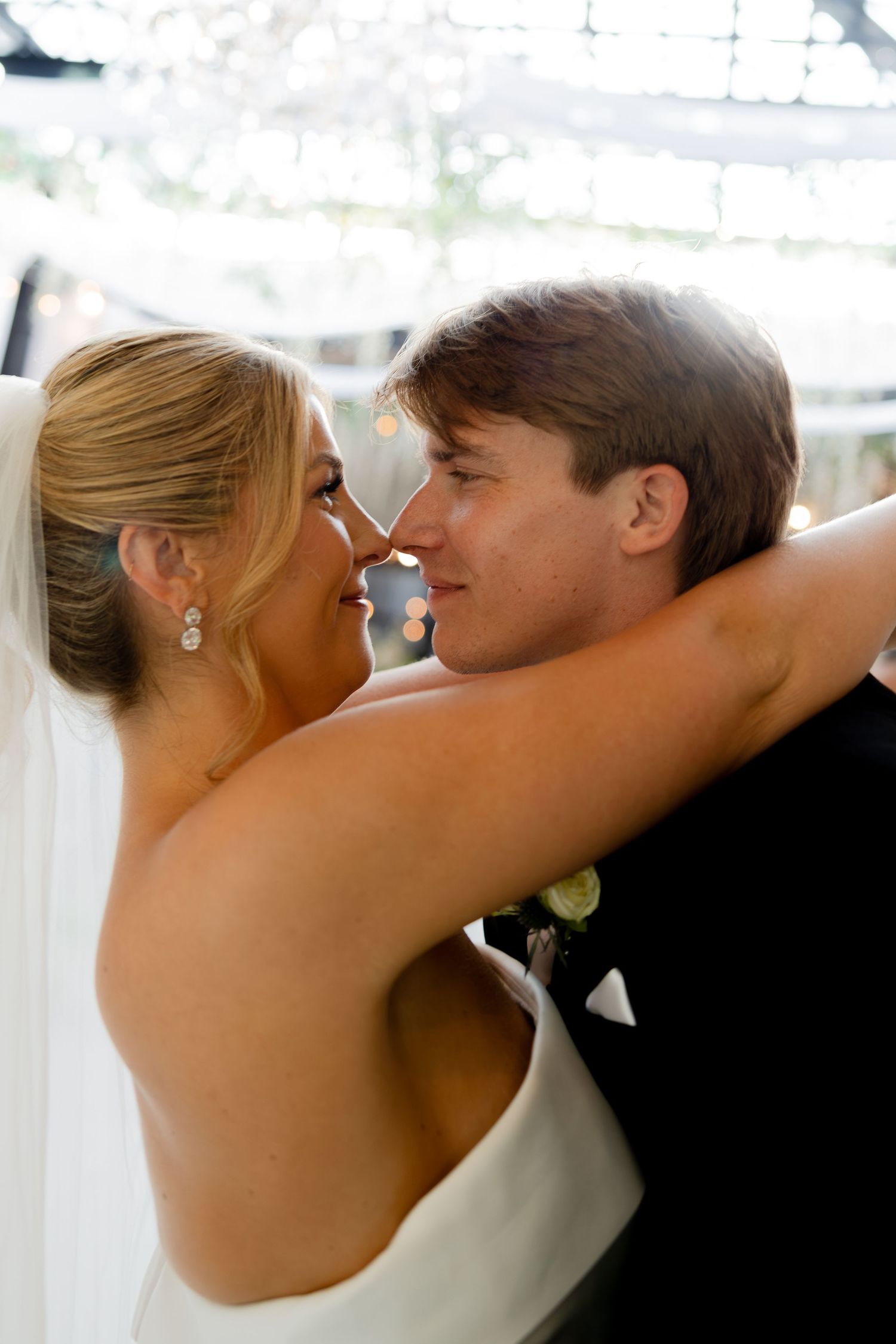 A bride and groom share an intimate moment, touching noses and smiling during their wedding reception dance.