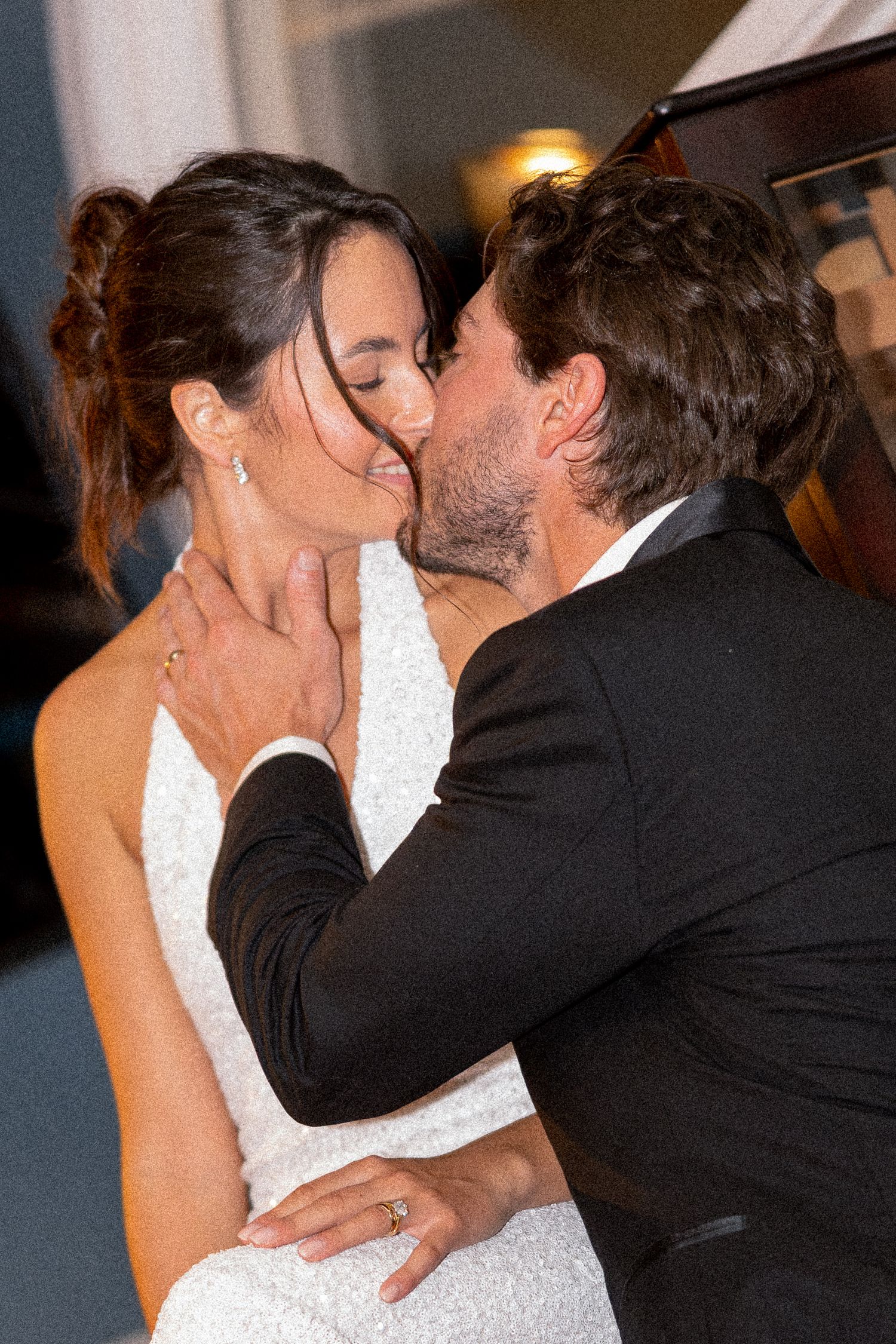 A couple shares a romantic kiss during their wedding reception, with the bride in a white gown and groom in a black tuxedo.