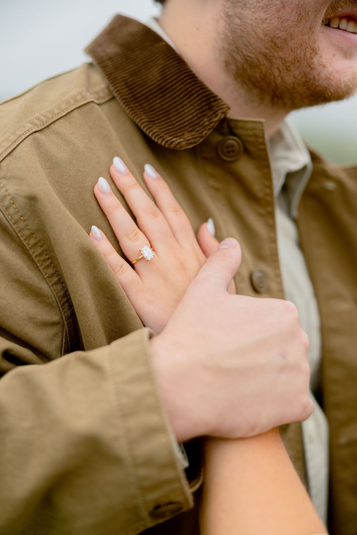 Close-up of a woman's hand with an engagement ring resting on a man's brown corduroy jacket.