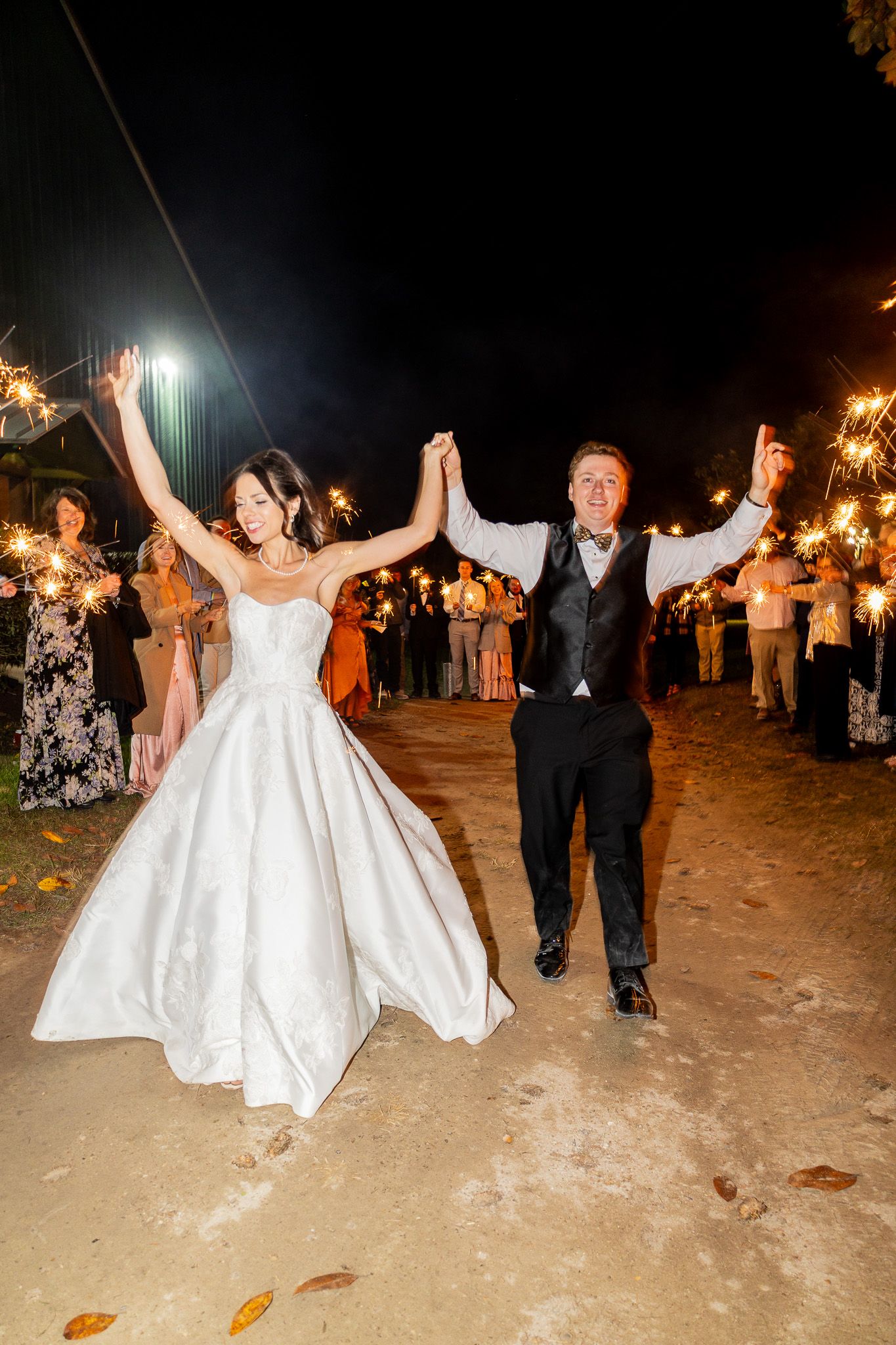 Bride and groom walk through sparkler exit at night wedding celebration with guests lining the path.
