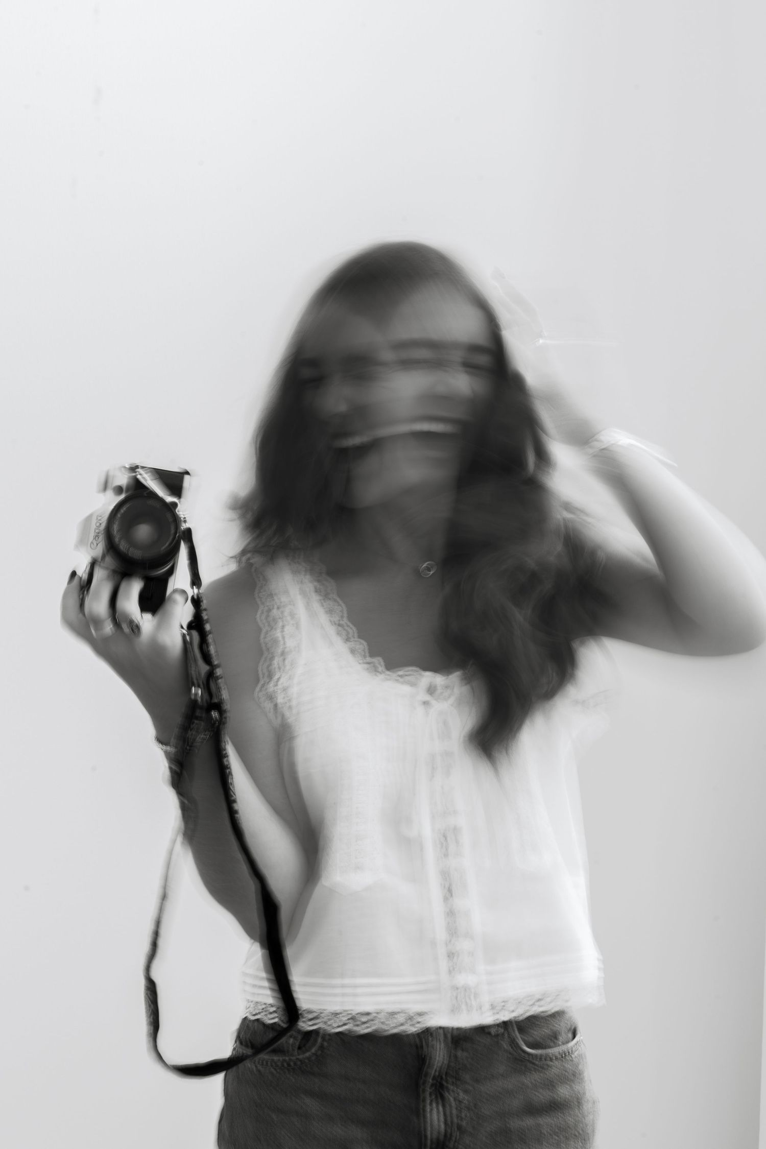 Black and white motion blur photo of a young woman holding a vintage camera, creating an artistic ghostly effect.