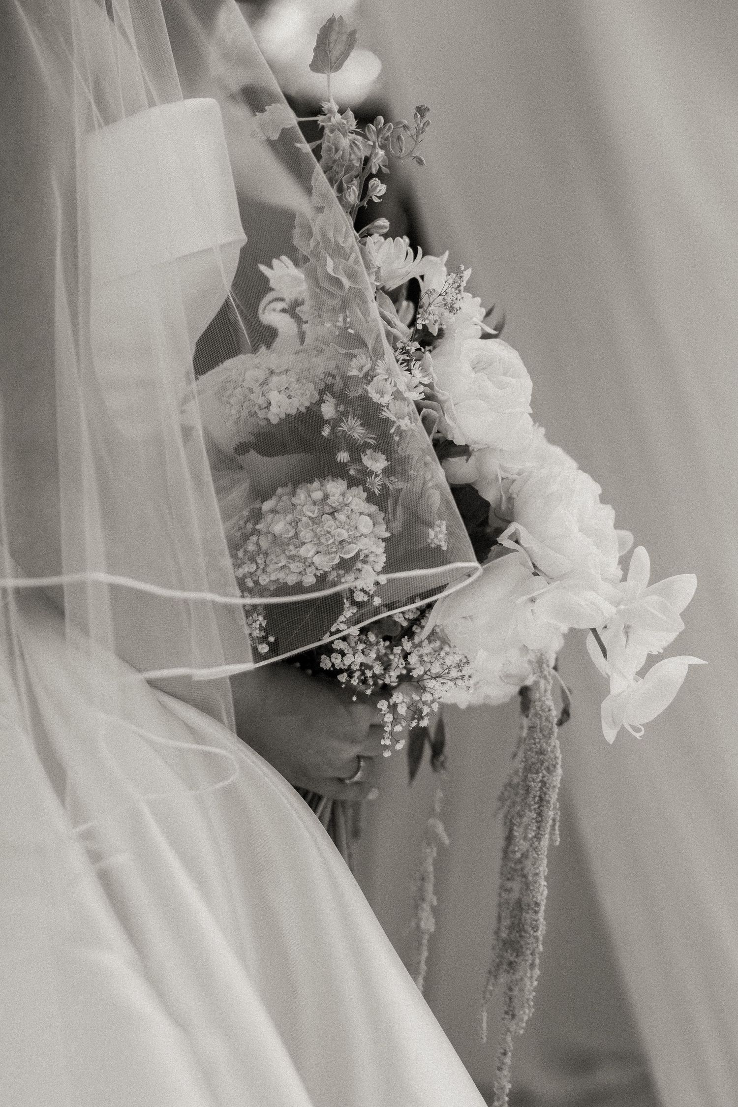 Black and white photo of a bride holding a floral bouquet with baby's breath, draped in a flowing veil.