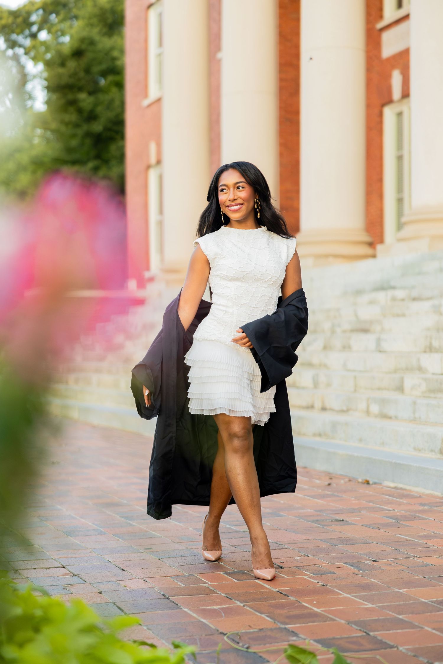 Woman in white ruffled dress and black coat walking on brick path near elegant building.