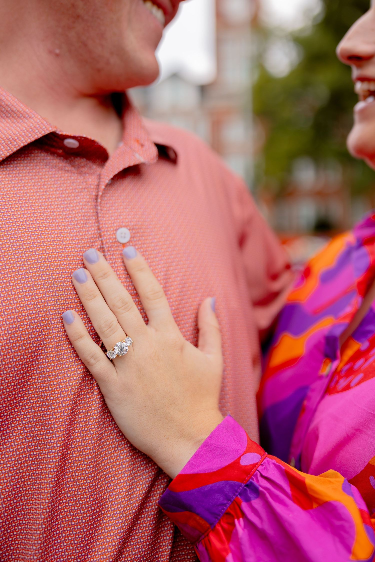 Close-up of a woman's hand with lavender nails and diamond engagement ring resting on a man's red shirt.
