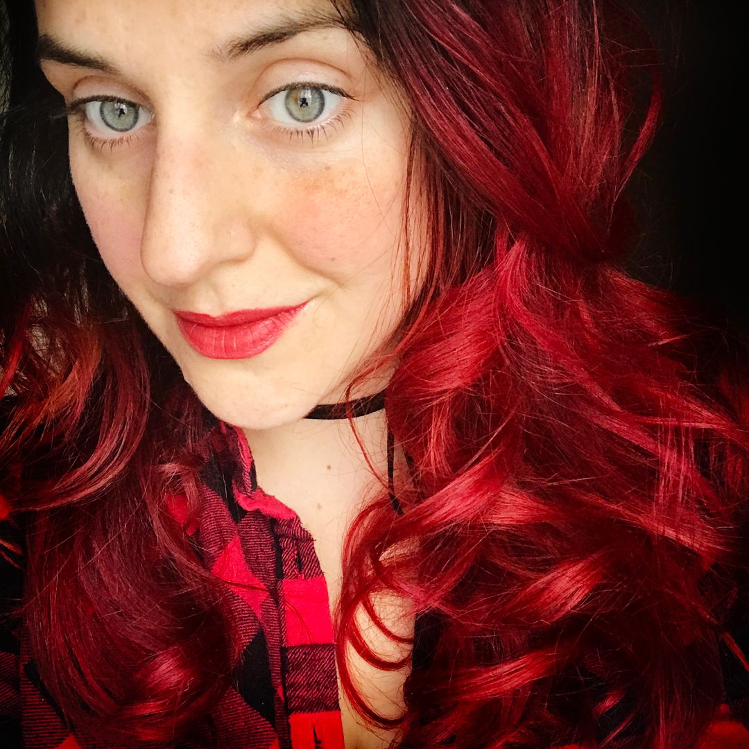 Portrait of someone with vibrant red hair and bright lipstick against dark background.