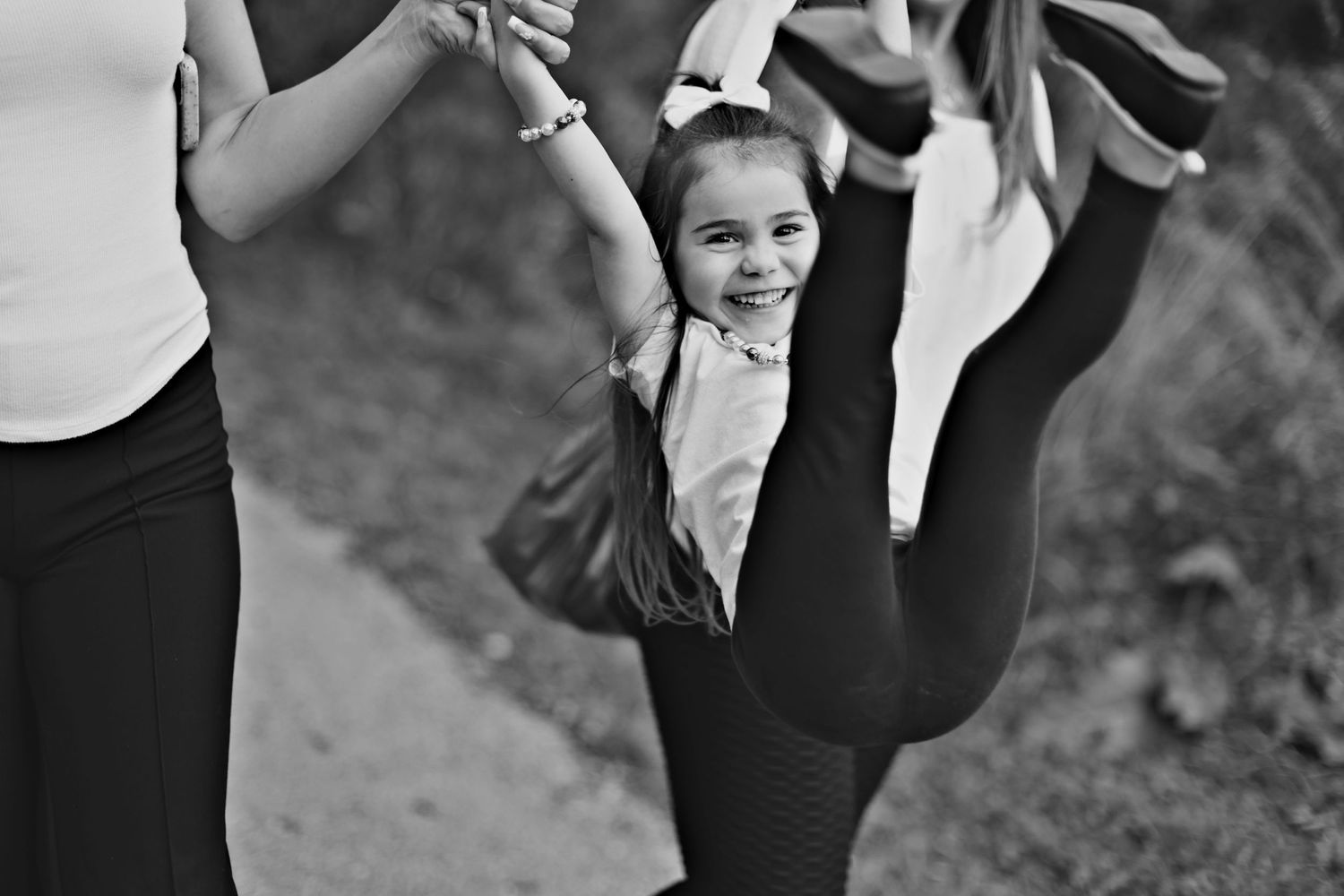 Young student in black leotard practices ballet leg extension with teacher guiding the movement.