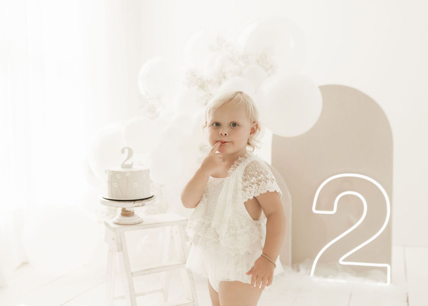 A person in white lingerie poses gracefully on a light-colored background in a minimalist studio setting.