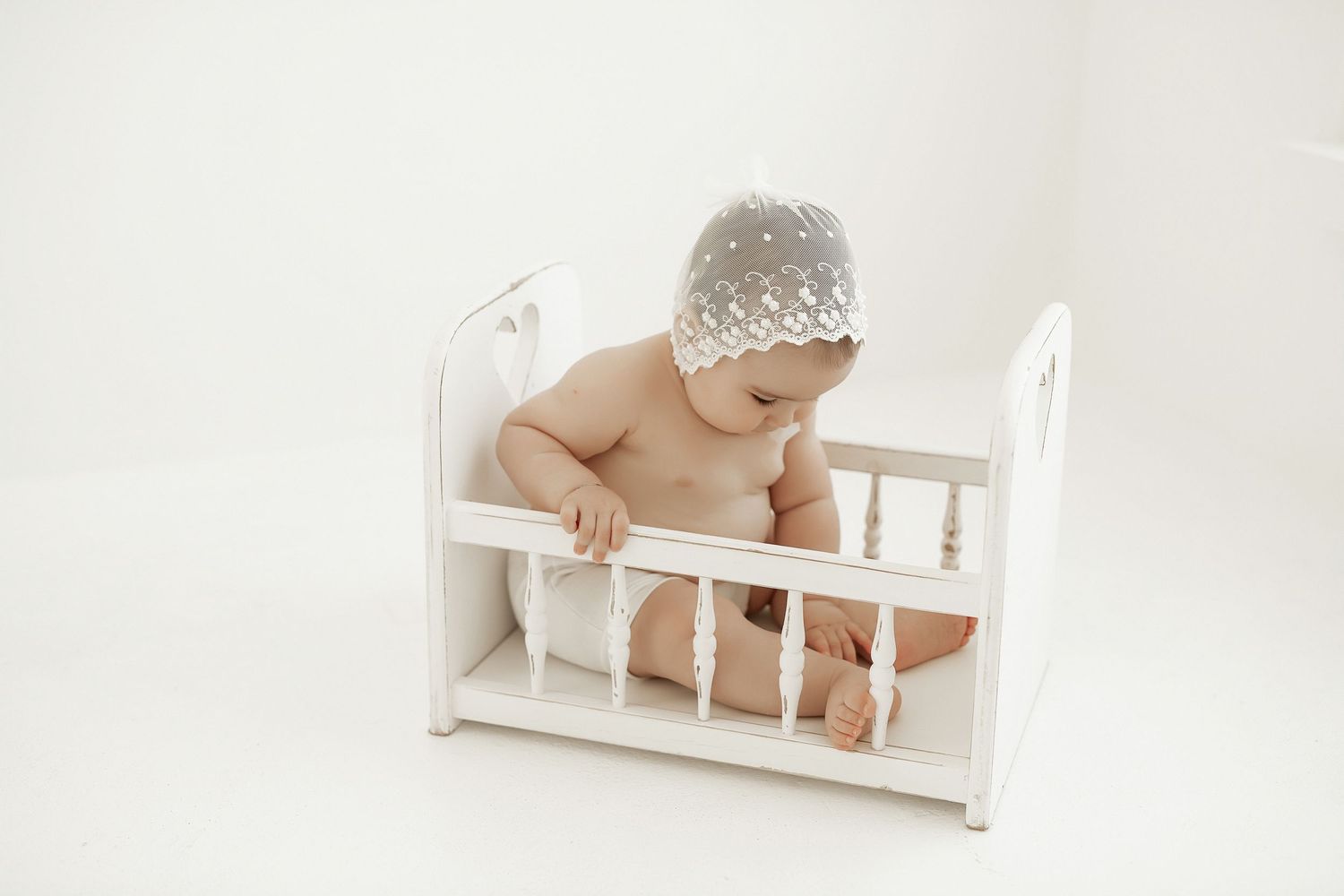 Baby in white clothing sits on floor with autumn leaves and candles creating cozy fall decor.