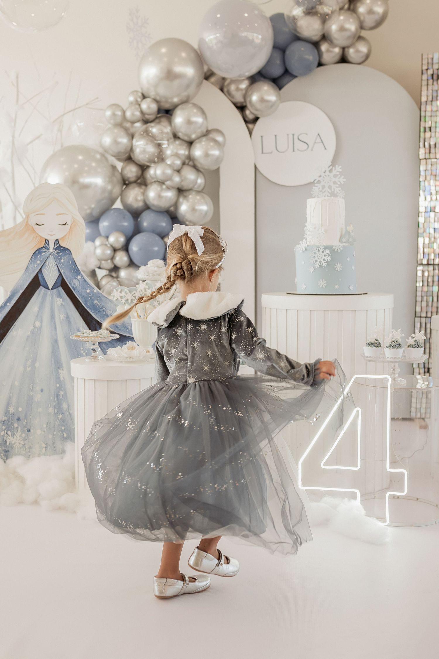 Elegant party decor featuring balloon arches in silver, blue and white with tulle dresses displayed against a white backdrop.
