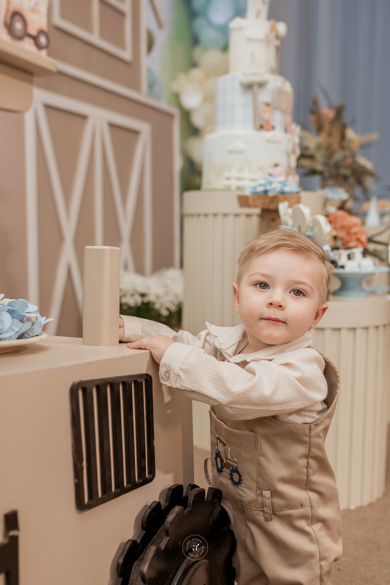 A baby in a beige outfit sits at a dining table with decorative elements in the background.