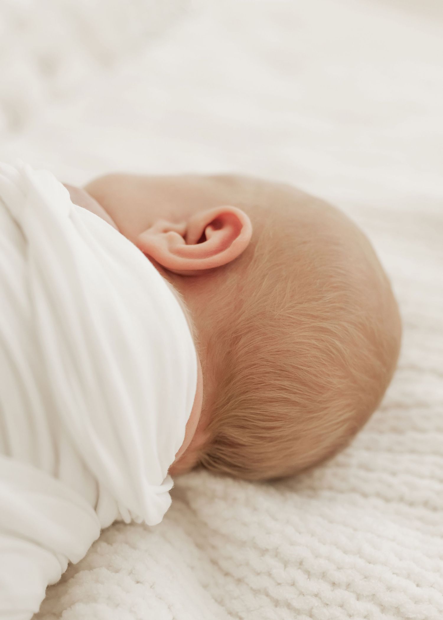 A sleeping baby in white clothing rests peacefully on a cozy knitted blanket.
