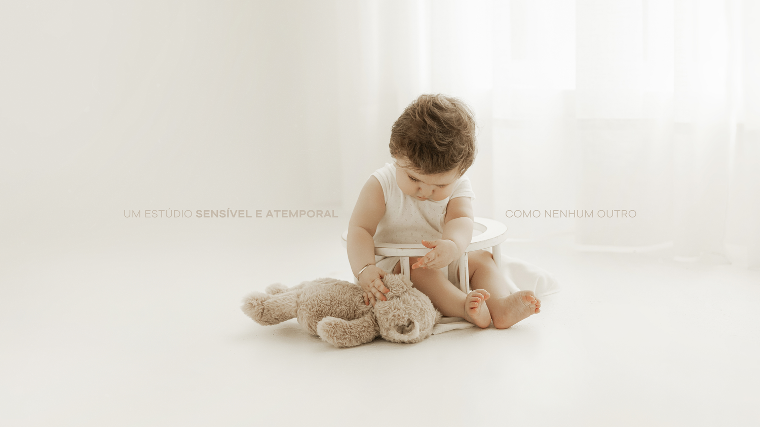 A baby in white clothing plays with a small stuffed animal toy on a bright white background.