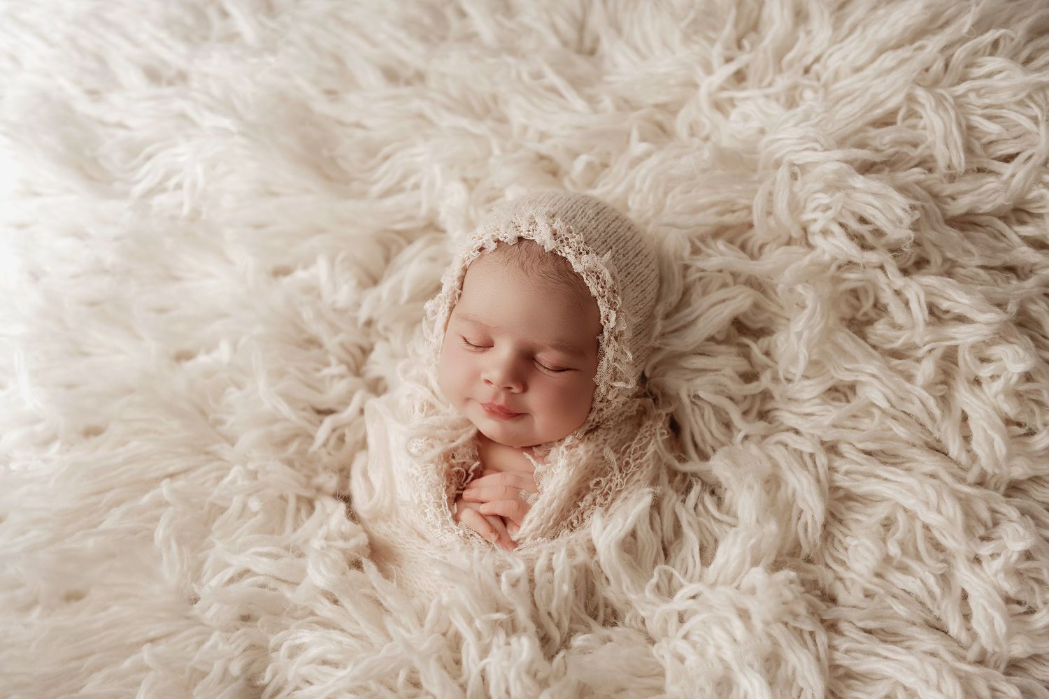 A sleeping newborn baby lies peacefully on soft white feathery fur blankets in a series of connected photos.