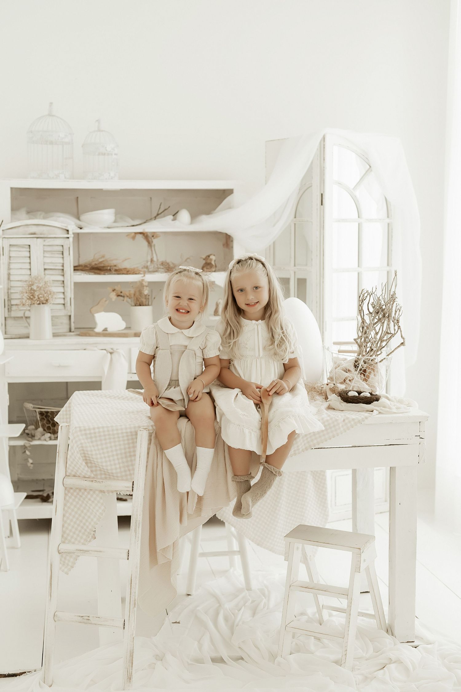 Children in white outfits sit at a rustic farmhouse table in a bright, airy white kitchen setting.
