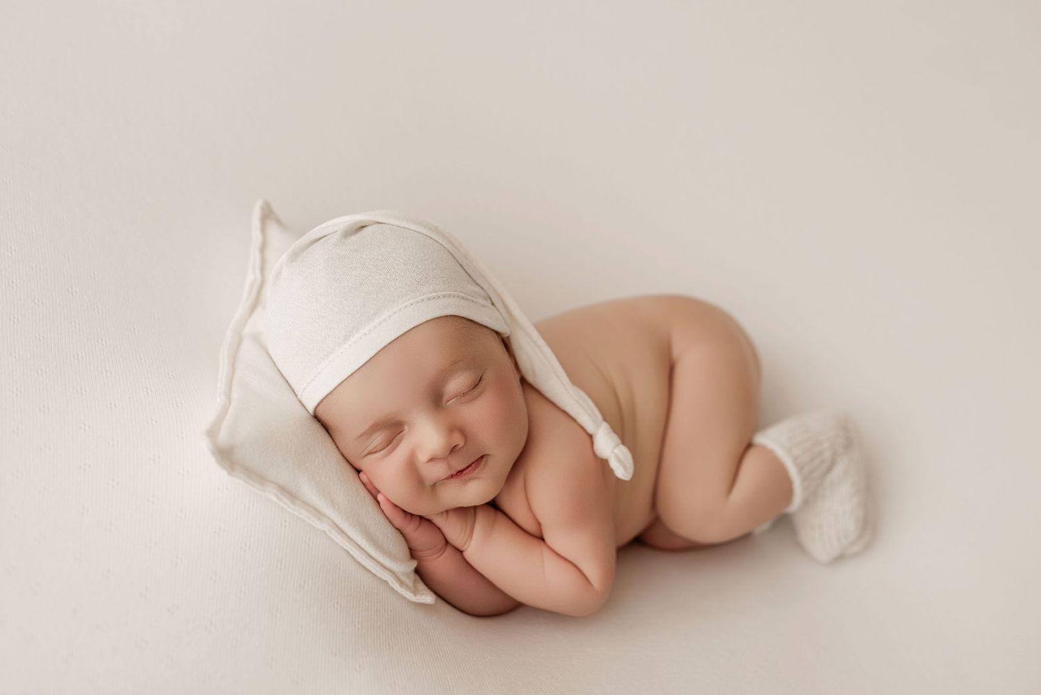 A series of minimalist newborn photography shots showing a sleeping baby in soft white tones against neutral backgrounds.