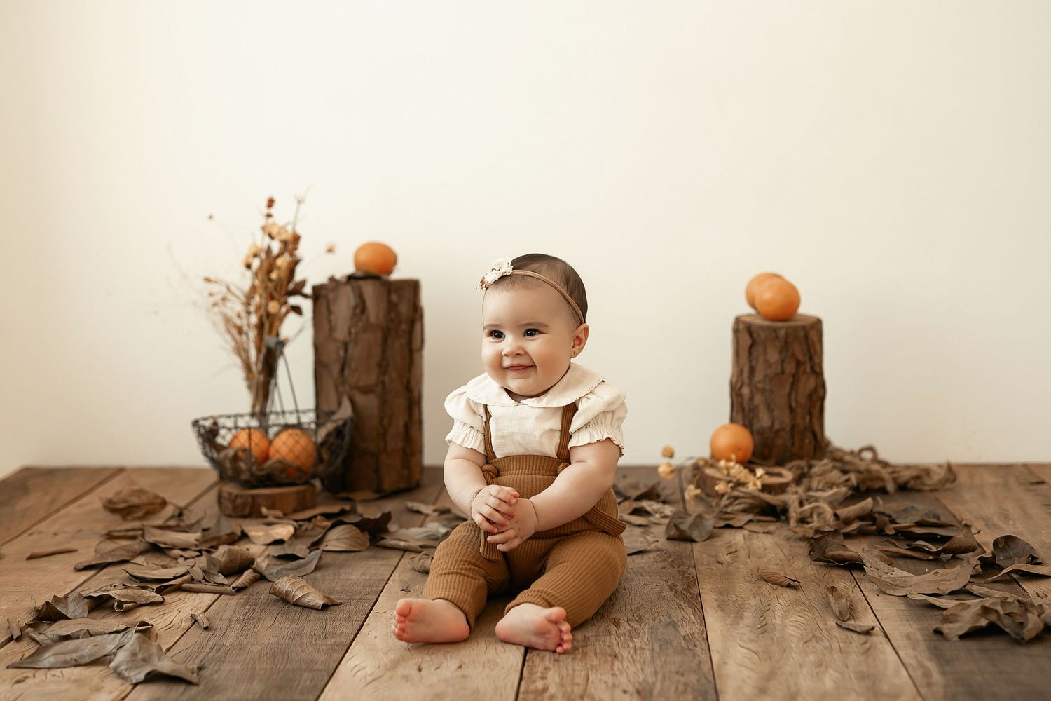 Baby plays with autumn leaves and wooden decor elements in minimalist fall photo setup.