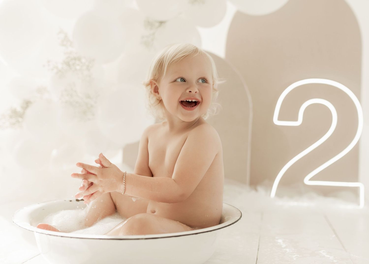 Baby sits in a white porcelain sink during bath time with joyful expression and wet hair.