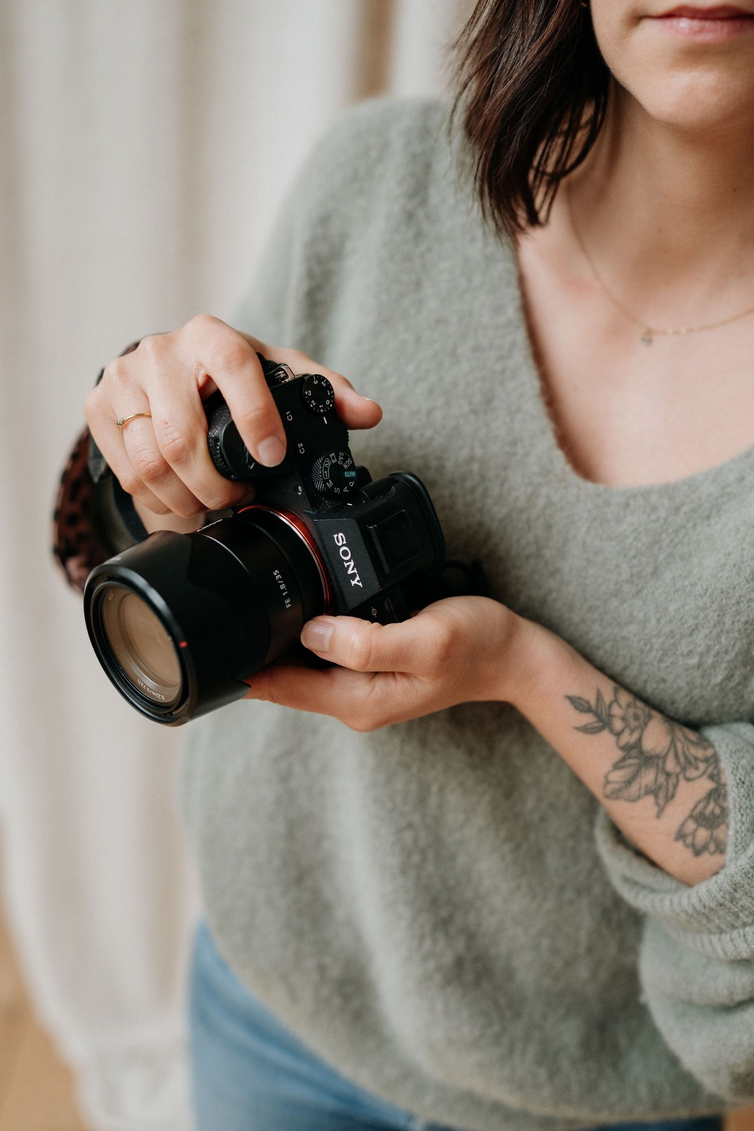 Close-up of hands holding a professional camera with a telephoto lens against a gray sweater.
