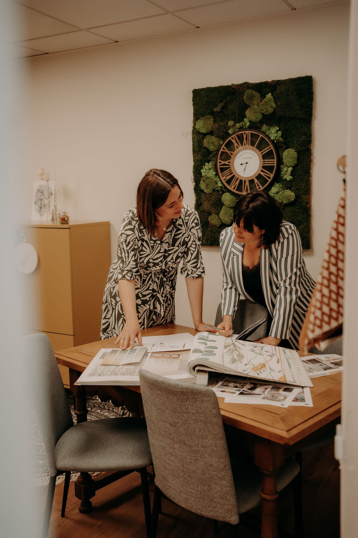 Business meeting between colleagues at wooden table with wall decor visible.