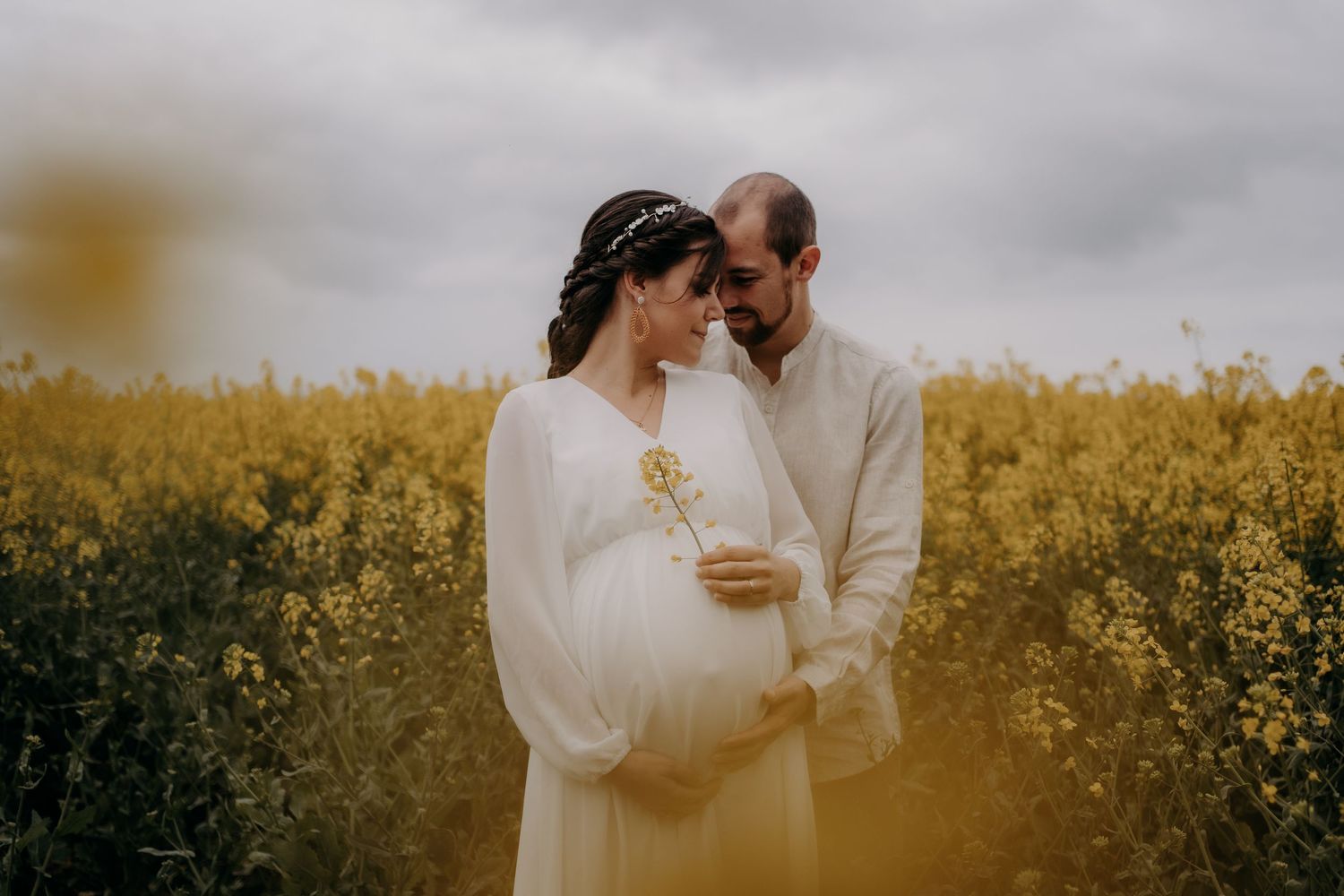 Couple sharing intimate moment in blooming yellow canola field during maternity photoshoot.