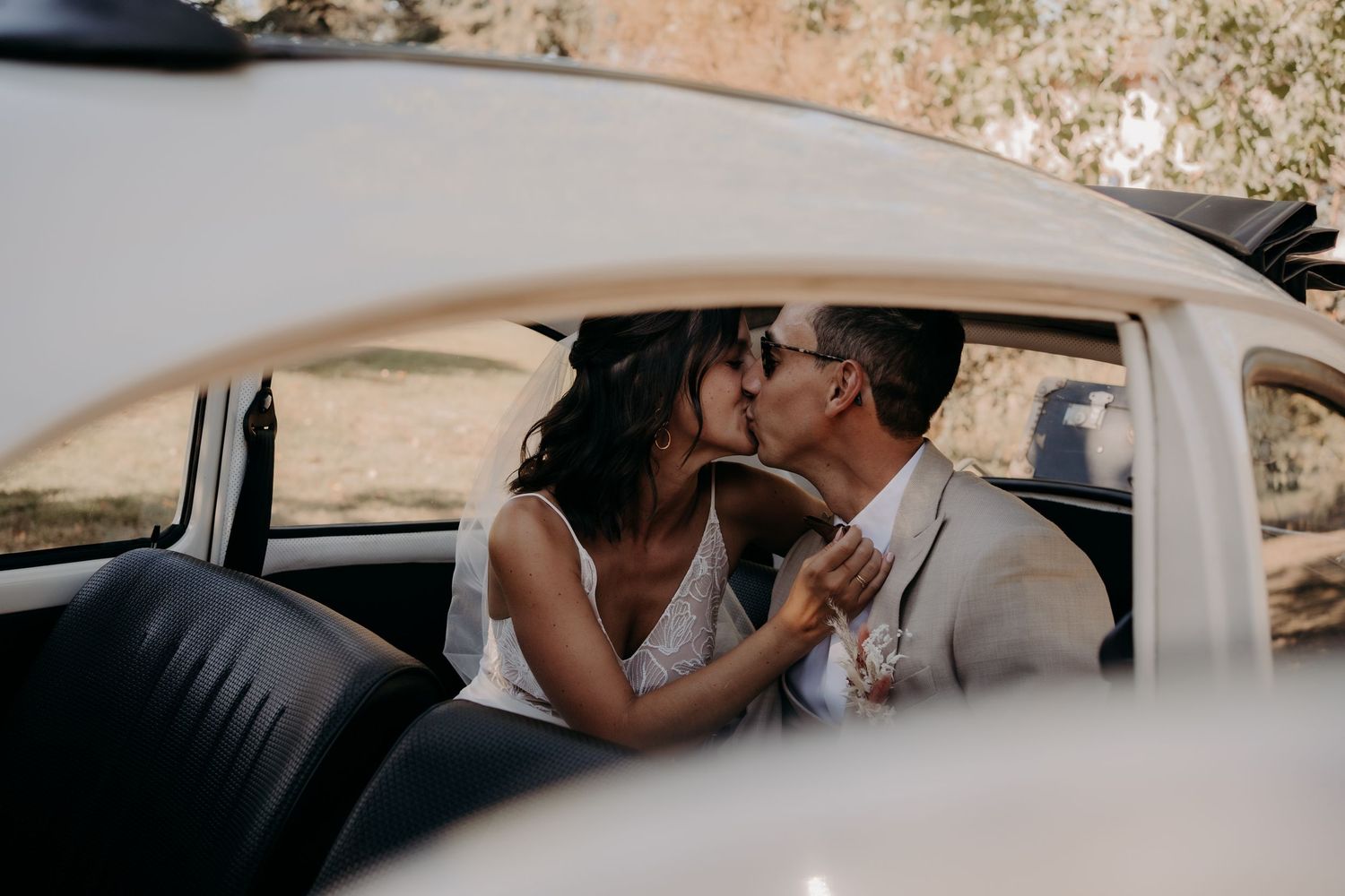 Romantic wedding couple shares a tender moment in a vintage car during sunset.