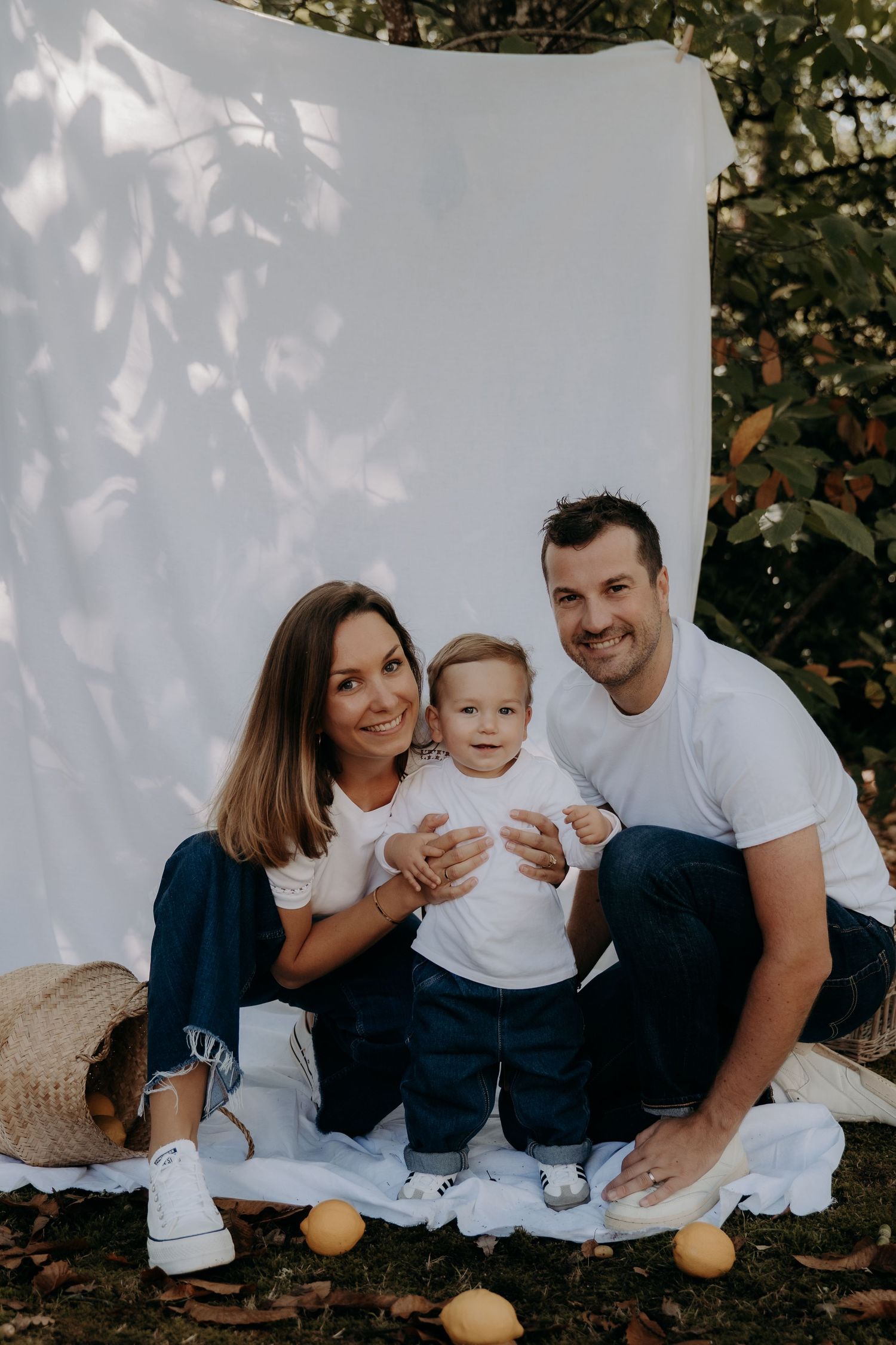 Family portrait against white backdrop with natural shadows and lemons scattered on ground.