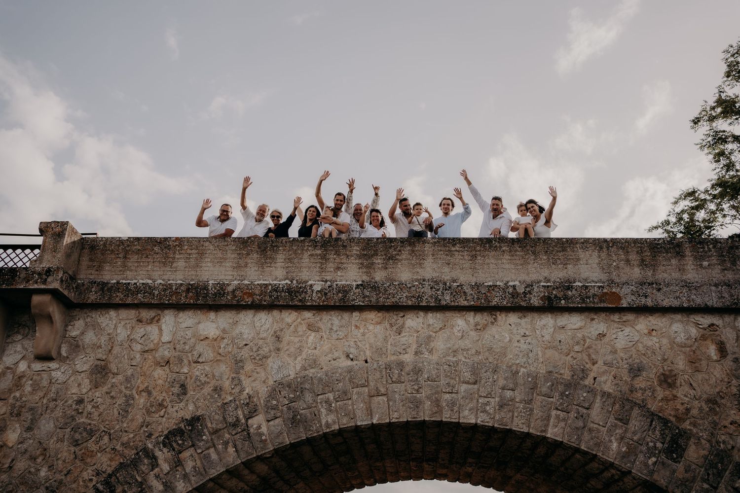 Celebratory group raising arms while standing on stone bridge.