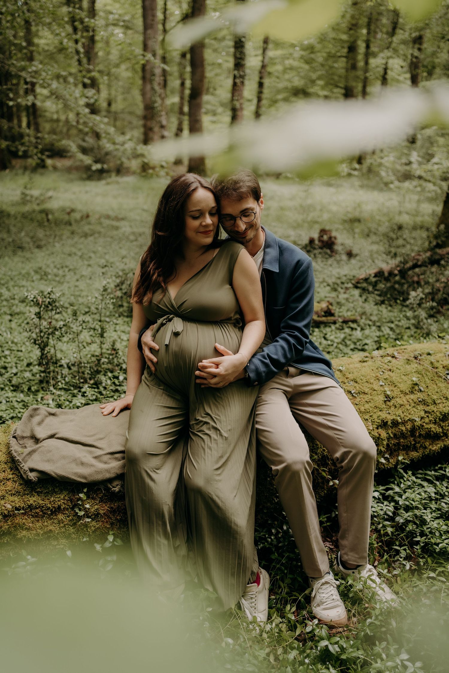 Maternity couple poses intimately in a lush green forest setting.