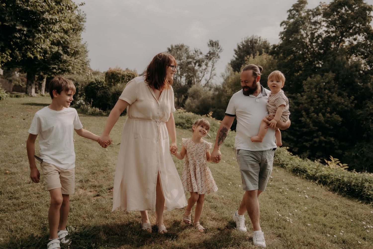 Family walking together hand in hand through a sunlit meadow during a golden hour photoshoot.