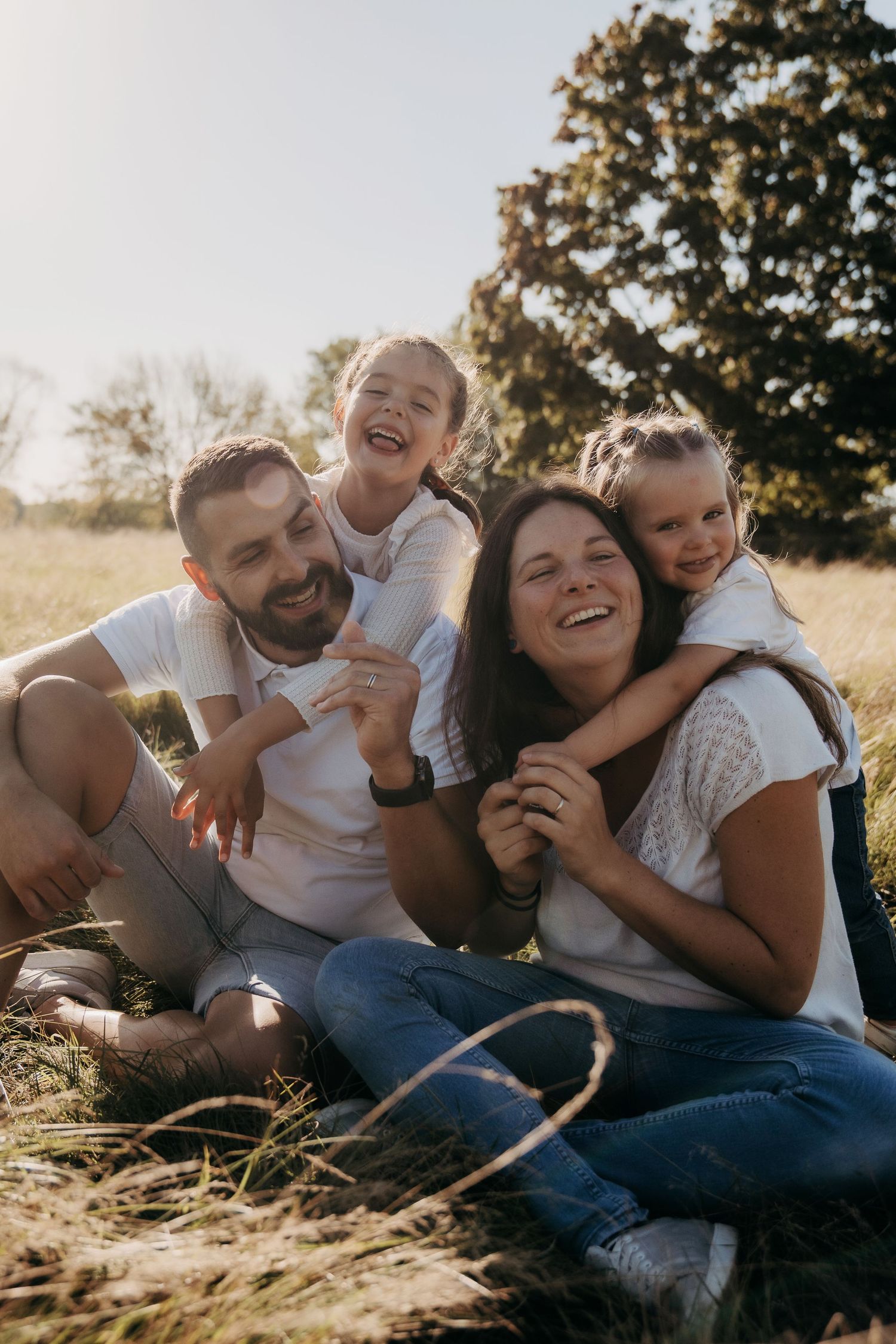 Happy family laughing and playing together while sitting in a sunny field during golden hour.