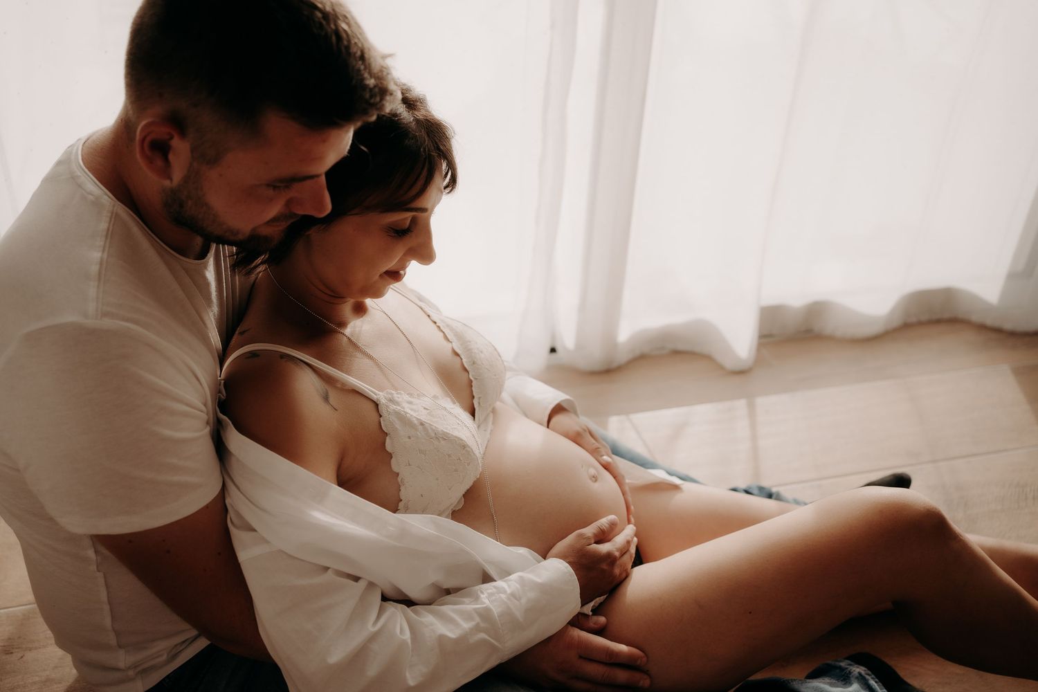 Intimate maternity photo of expectant couple embracing in soft window light.