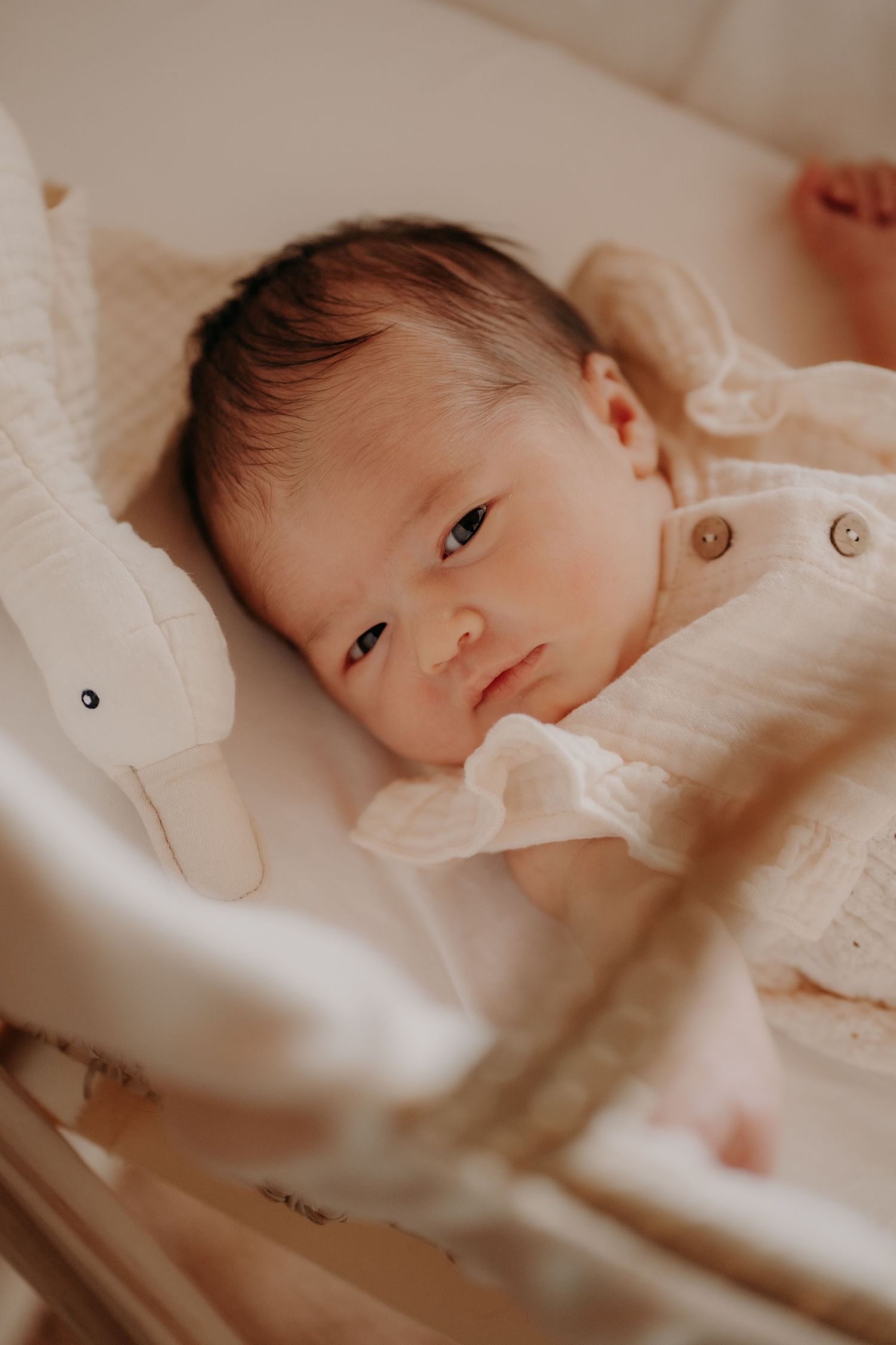 Close-up view of baby lying in white crib beneath mobile toys.
