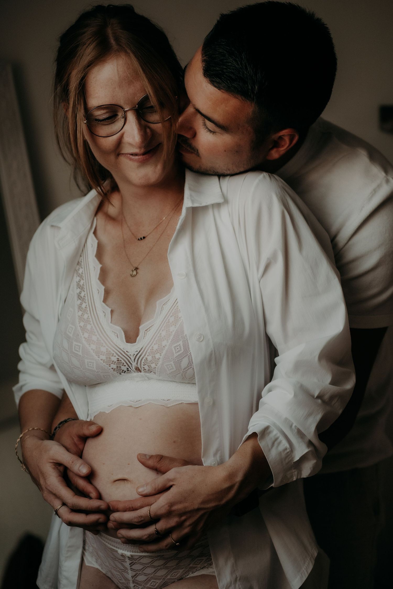 Intimate maternity photoshoot showing tender moments between expectant parents in moody lighting.