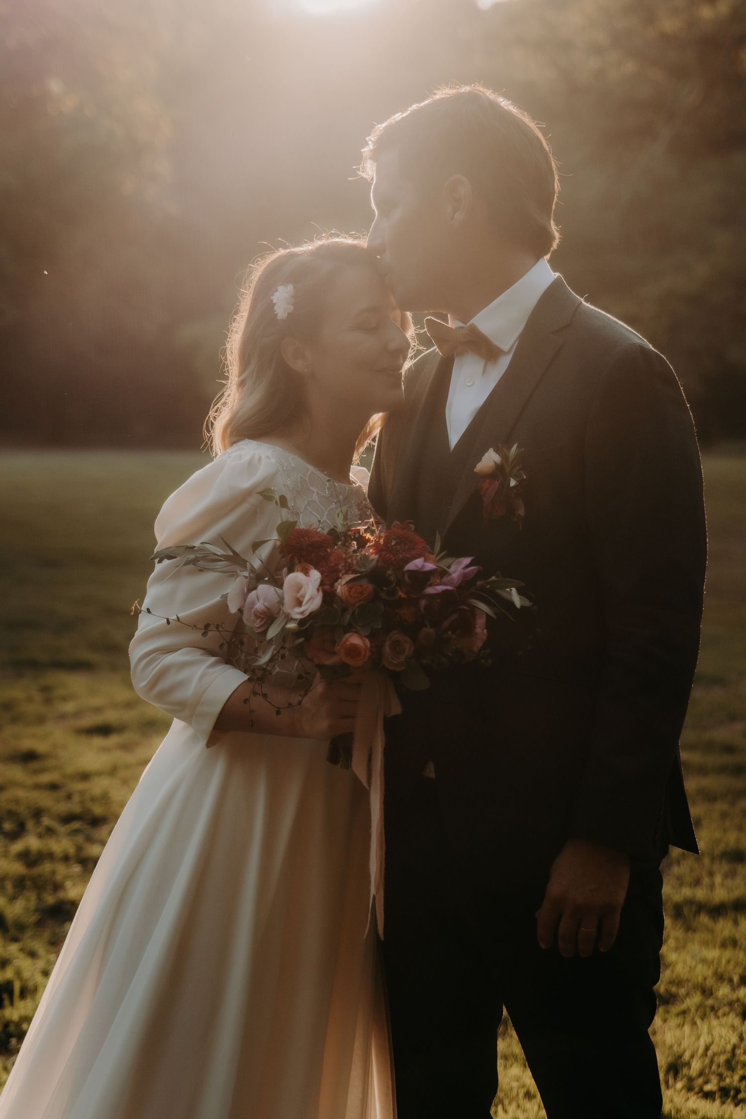 Silhouetted couple in wedding attire stands together in warm sunset lighting.