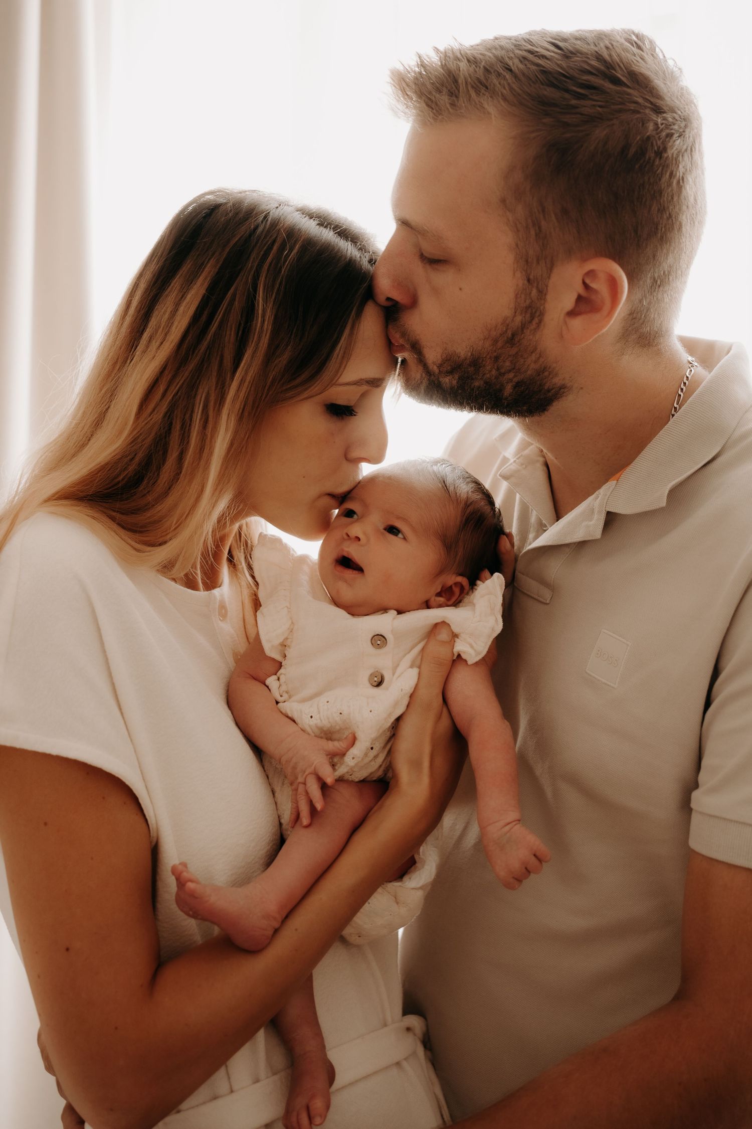 Indoor family photoshoot with soft lighting capturing loving interactions in white attire.