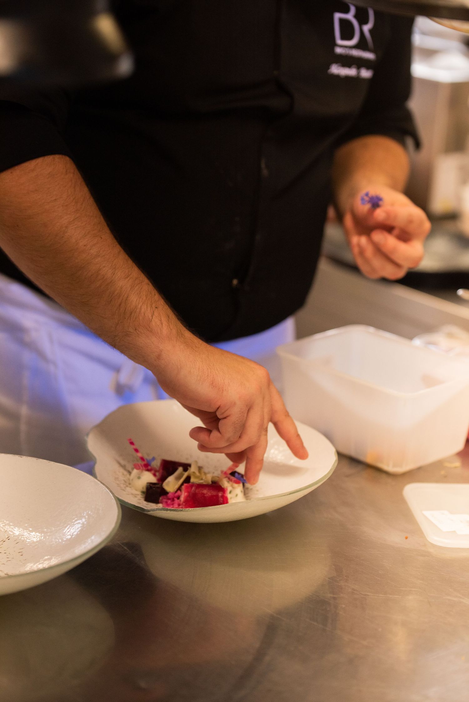 Chef hands plating food on white dishes in a professional kitchen setting.